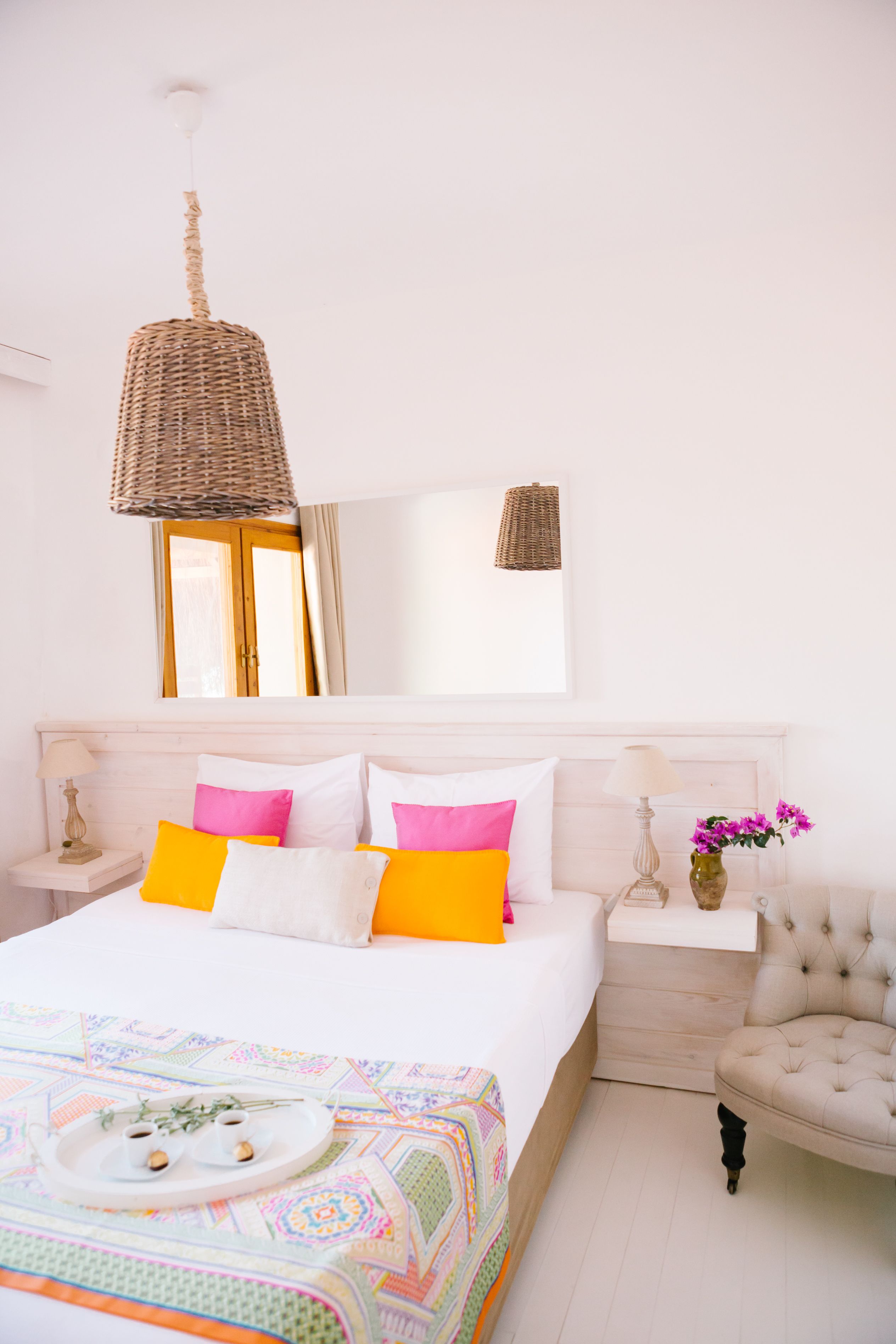 A bedroom with a bed, bedside tables, a hanging light fixture, a chair, and a window.