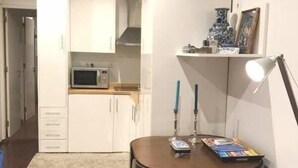 A compact living space with a kitchenette, a dining table with chairs, and a small side table with a lamp and decorative items.