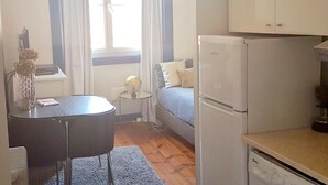A compact kitchen with a refrigerator, a small dining table, and a window with curtains.