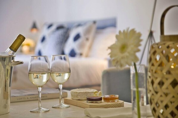 A table with two glasses of white wine, a cheese platter, and a candle.