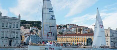 A sailboat named 'De Plano' on a body of water with buildings in the background.
