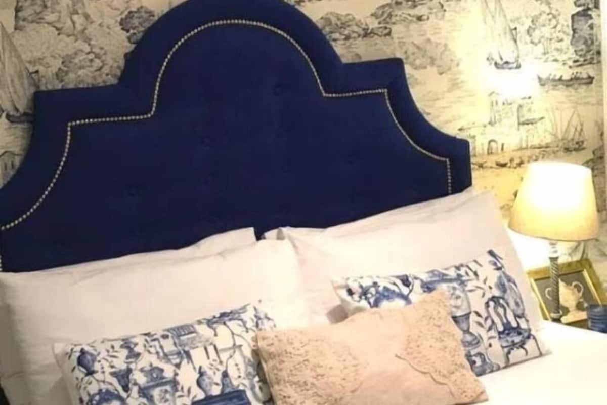 Una cama con cabecera azul oscuro, varios almohadones y un papel tapiz estampado.