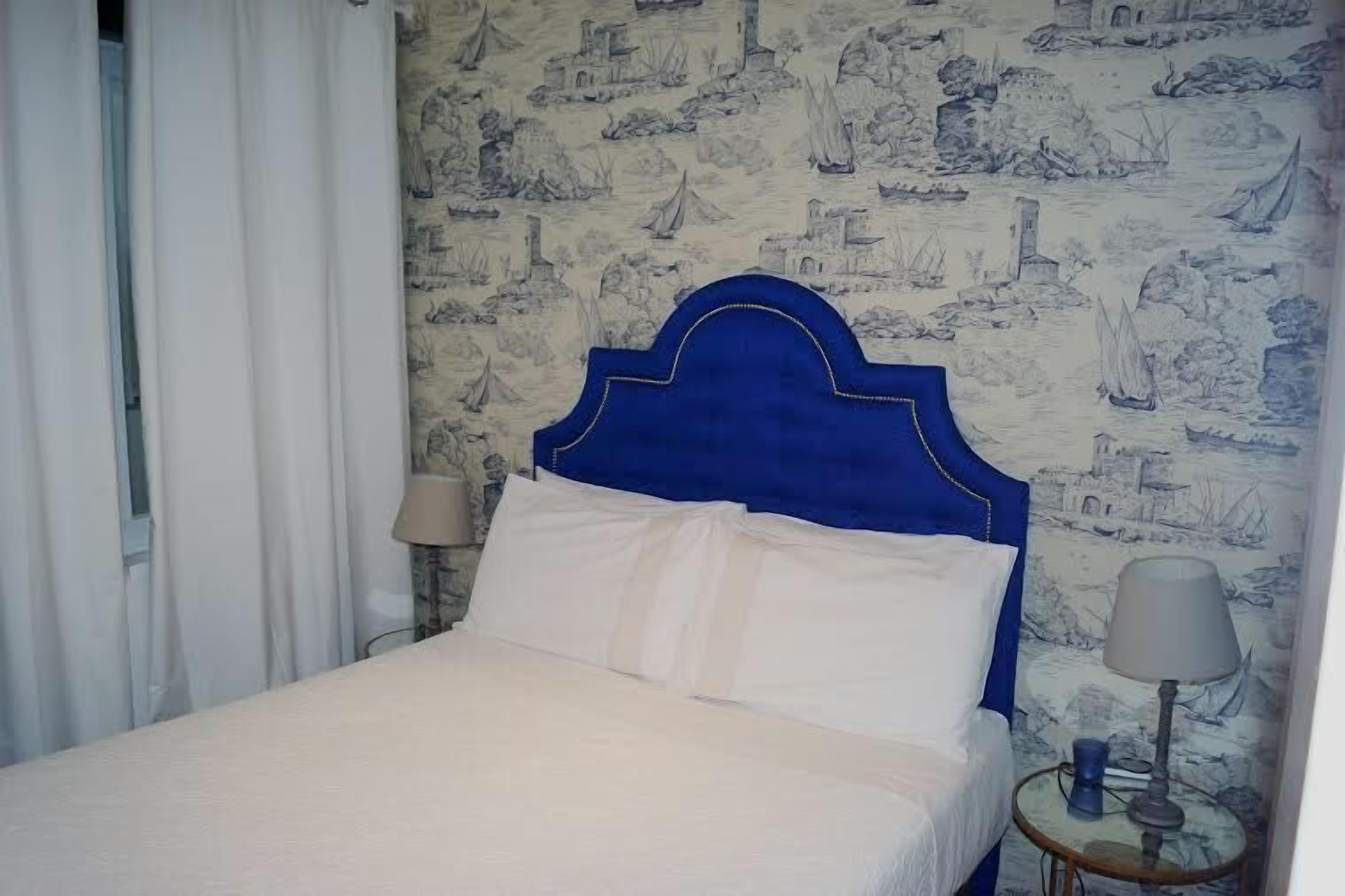 A bedroom with a blue headboard, white bedding, and a wall with nautical-themed wallpaper.