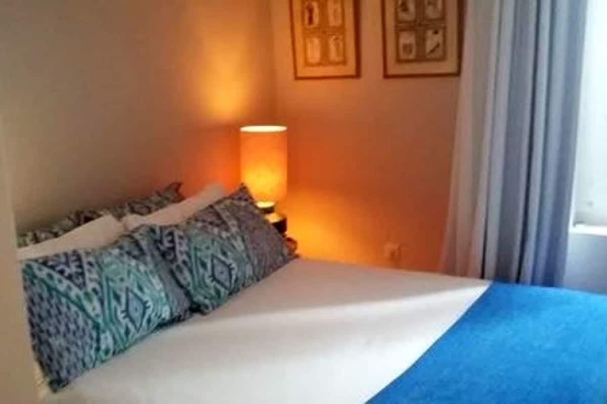 Una habitación de hotel con cama, almohadones estampados, lámpara de noche y cortinas.