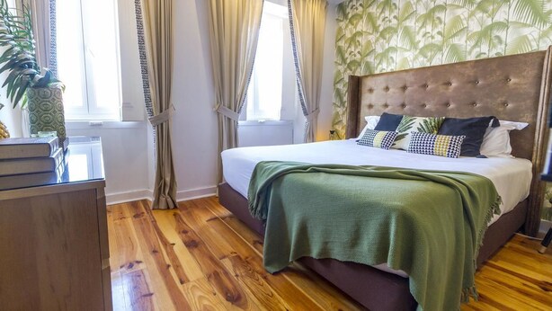 A bedroom with a large bed, a wooden dresser, and a window with curtains.