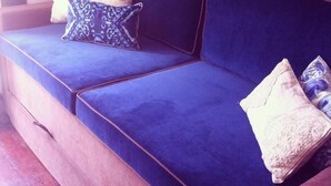 A blue sofa with three pillows, one patterned and two plain, in a room with a textured wall.