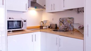 A modern kitchen with white cabinets, a microwave, a coffee maker, and a patterned backsplash.