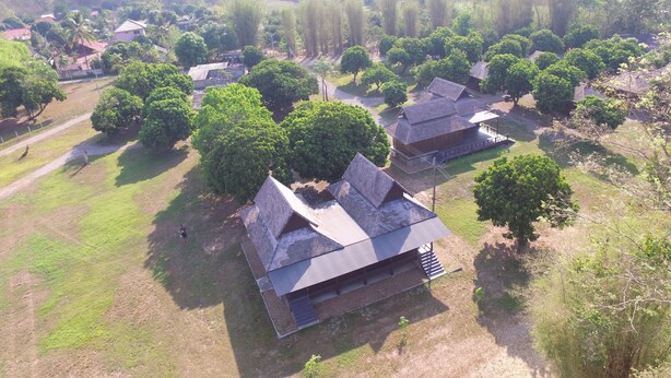 Vista aérea de uma área rural com casas tradicionais, rodeada por vegetação exuberante e árvores.