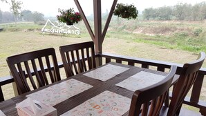 Uma mesa de jantar de madeira com quatro cadeiras, um estojo de lenços de papel e um letreiro com vista para um campo gramado e árvores.