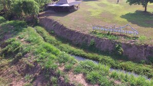 Paisagem rural com uma casa, uma área cercada e um pequeno riacho.