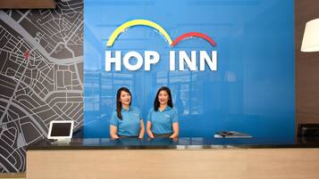 Un mostrador de recepción con un gran letrero azul que dice "HOP INN" y dos empleados detrás.