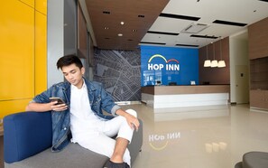 A man sitting on a bench in a modern lobby with a reception desk labeled "HOP INN". - Hop Inn Hotel Makati Avenue (Makati)