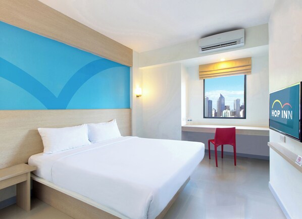 Quarto de hotel com cama, escrivaninha, cadeira, televisão e janela com vista para a cidade.