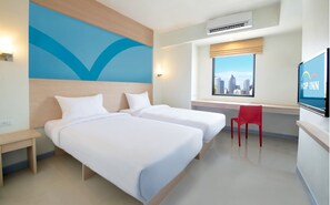 Quarto de hotel com duas camas, uma escrivaninha, uma cadeira vermelha, uma televisão e vista para a cidade.