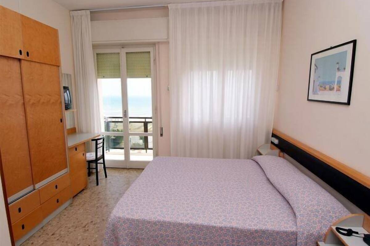 A hotel room with a bed, a desk, a chair, and a wardrobe.