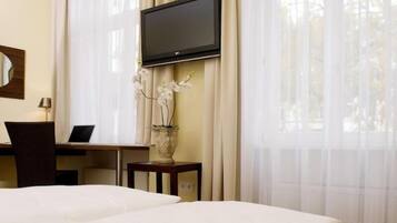 A hotel room with two beds, a desk with a laptop, a television mounted on the wall, and a vase with white flowers.