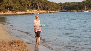 Eine Person geht an einem Strand entlang, im Hintergrund Wasser und Bäume.