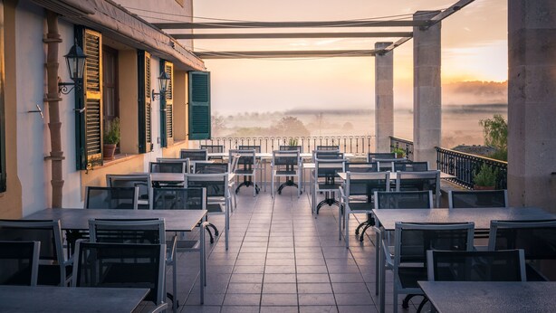 Eine Terrasse im Freien mit Tischen und Stühlen, mit Blick auf ein Gewässer und eine neblige Landschaft.