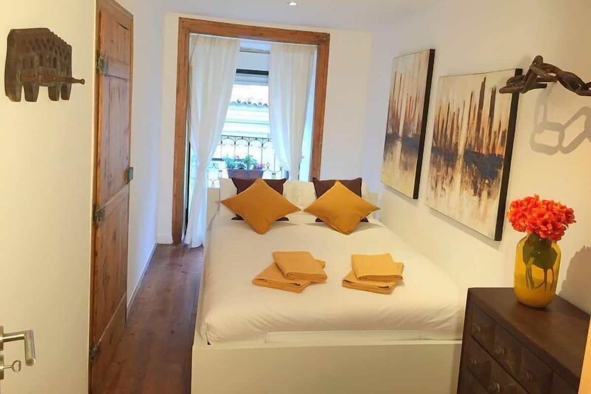 Une chambre à coucher avec un lit, des oreillers, une table de chevet et des œuvres d’art accrochées au mur.