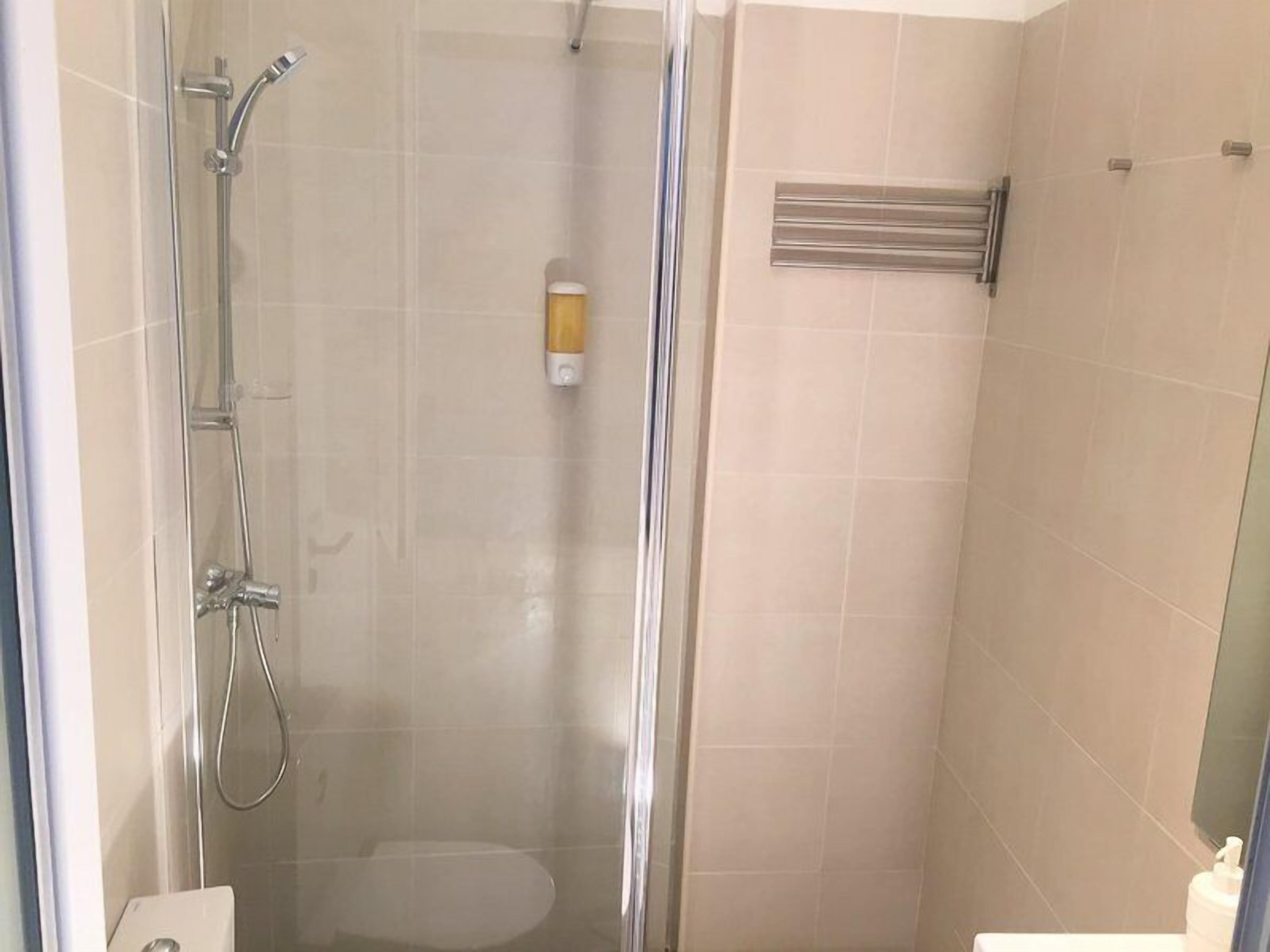 A glass-enclosed shower with a handheld showerhead and a wall-mounted faucet.