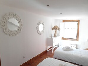 A bedroom with two beds, a white dresser, and two ornate mirrors on the walls.