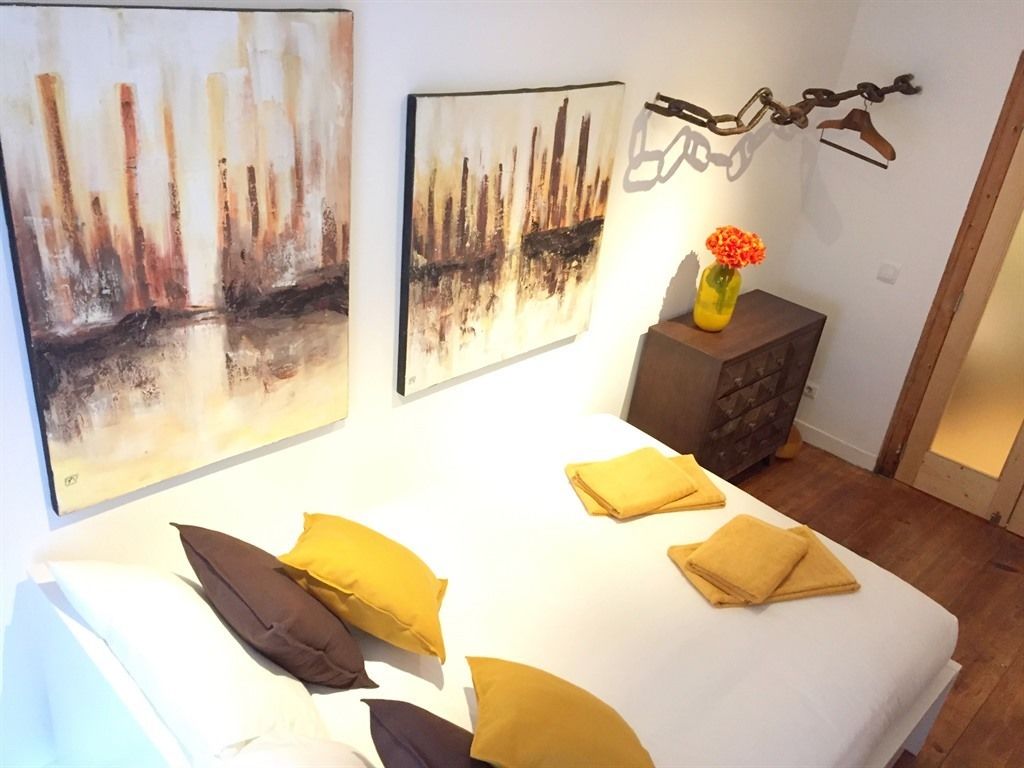 A bedroom with a large bed, multiple pillows, a dresser, and two abstract paintings on the wall.