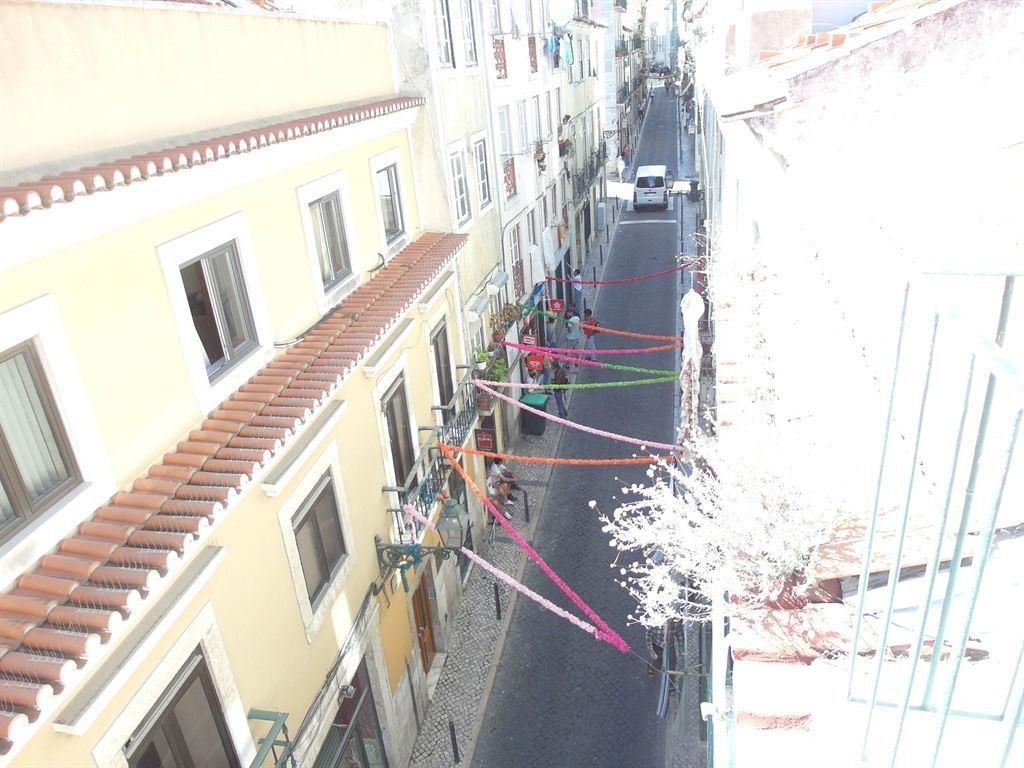 Una calle estrecha flanqueada por edificios, con balcones y una camioneta blanca estacionada a la derecha.