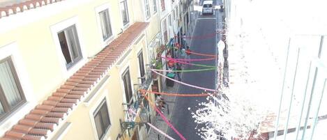 Una calle estrecha flanqueada por edificios, con balcones y una camioneta blanca estacionada a la derecha.