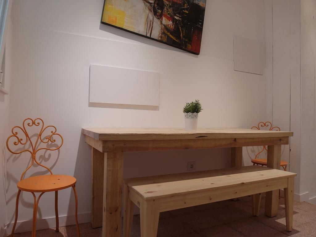 A wooden table with a bench, two metal chairs, a small potted plant, and a blank whiteboard on the wall.