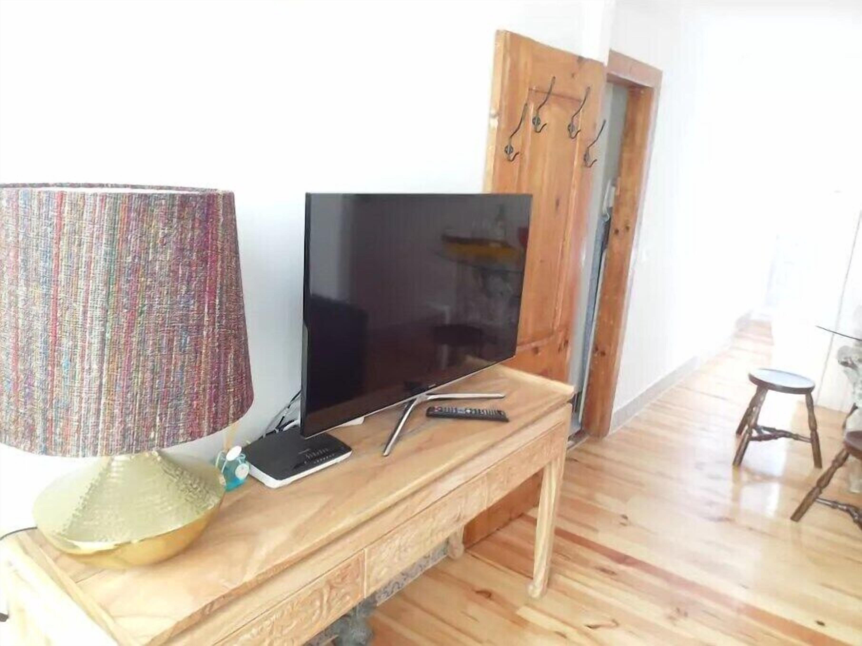 A wooden TV stand with a flat-screen TV, a lamp, and a remote control.
