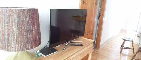 A wooden TV stand with a flat-screen TV, a lamp, and a remote control.