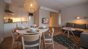 A modern kitchen with white cabinets, a dining table with chairs, and a hanging light fixture. - Simloc Hotel Drottninggatan (Arjeplog)