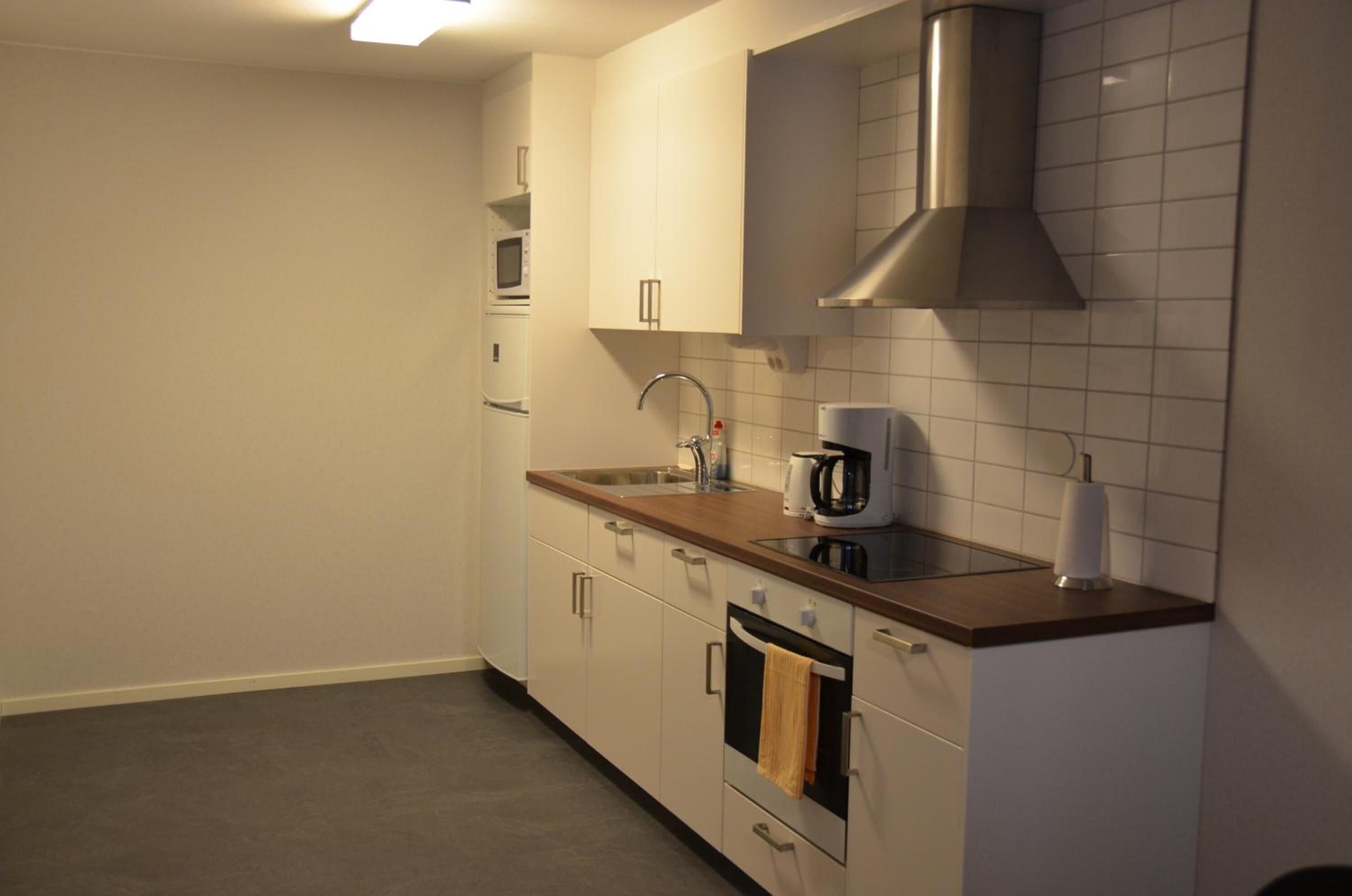 A modern kitchen with white cabinets, a stainless steel range hood, a sink, and a microwave.
