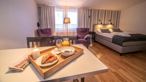 A hotel room with a bed, two armchairs, a dining table with breakfast, and a window with curtains. - Simloc Hotel Drottninggatan (Arjeplog)