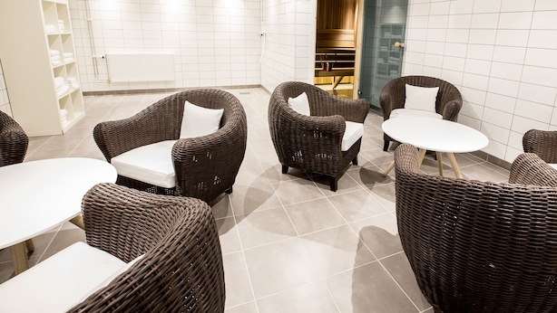 A modern indoor space with wicker furniture, white tiled walls, and a glass shower enclosure. - Simloc Hotel Drottninggatan (Arjeplog)