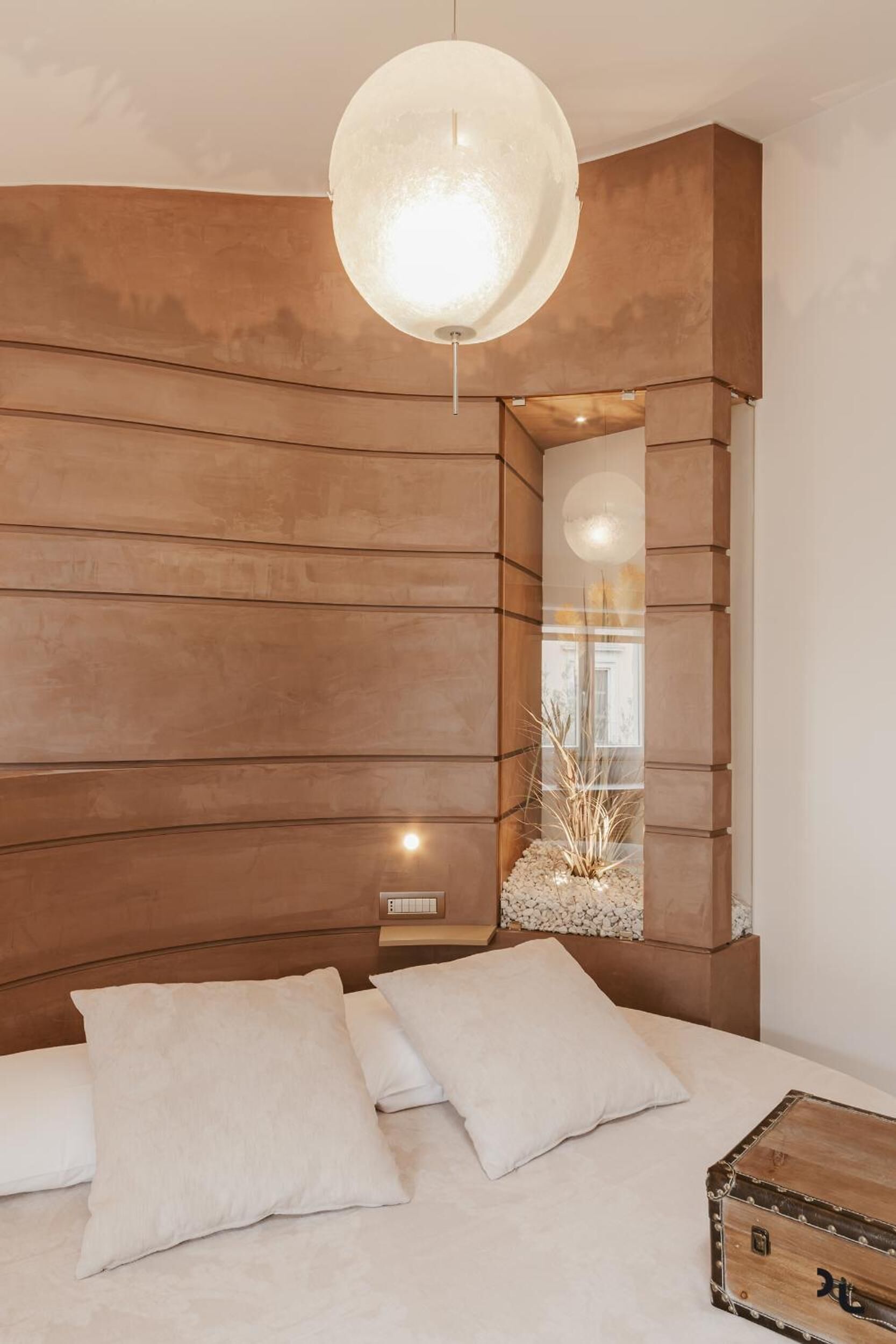 Un dormitorio moderno con cabecera de madera, una lámpara colgante redonda y una mesita de noche con un adorno.
