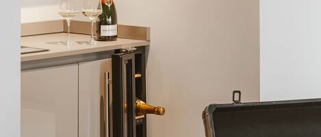 A room with a bed, a chest of drawers, a suitcase, and a bottle of champagne.