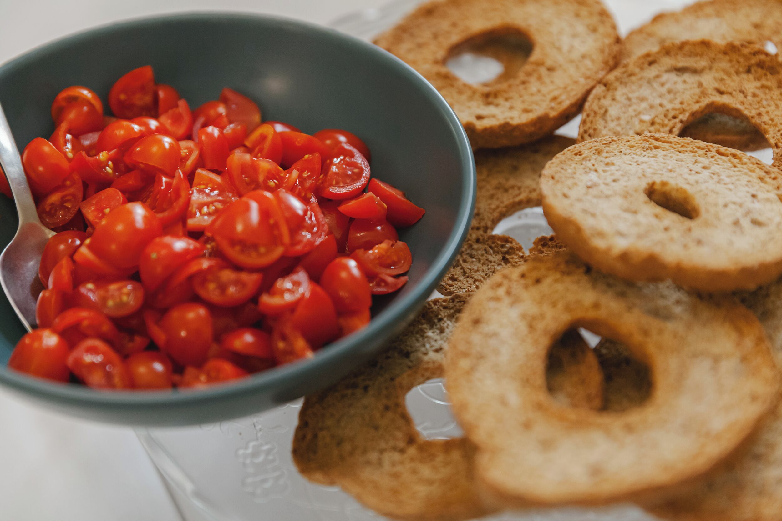 En skål med skivade tomater och bagels på en vit yta.