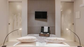 A modern bedroom with a bed, a flat-screen TV, a bedside table, and two floor lamps.
