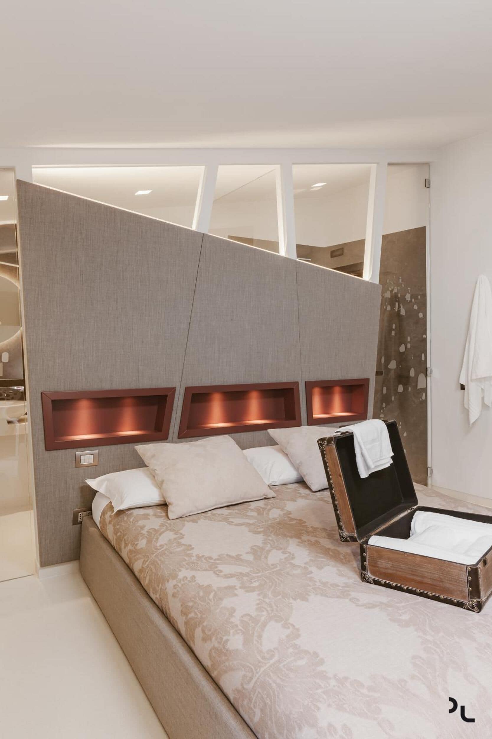 Een moderne slaapkamer met een groot bed, inbouwverlichting en een decoratieve spiegel.