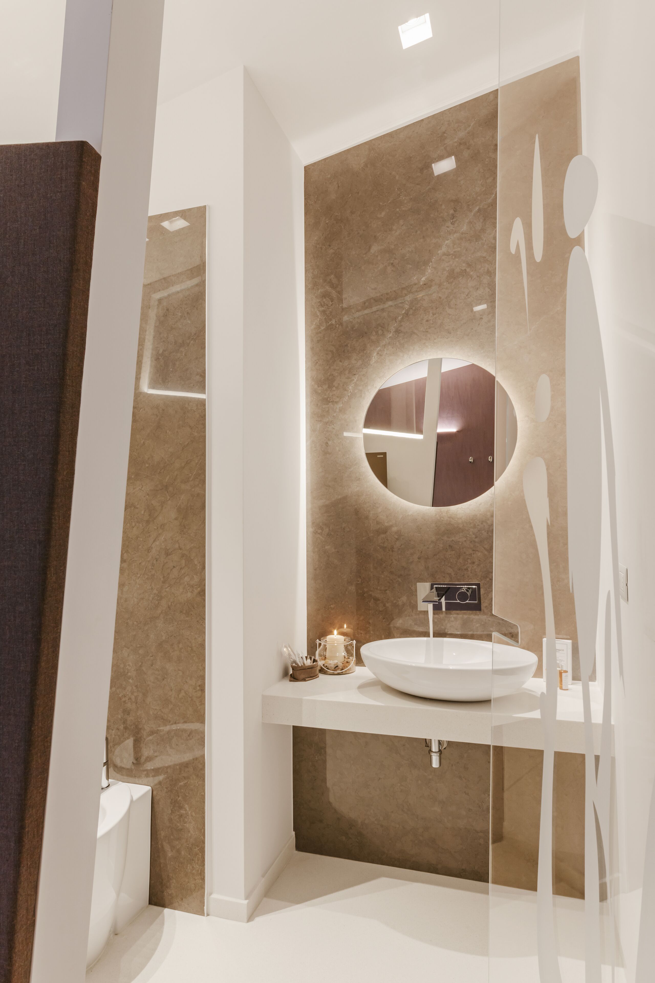 Ein modernes Badezimmer mit einem runden Spiegel, einem weißen Waschbecken und einer beige gefliesten Wand.