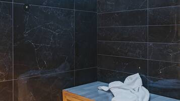 Een badkamer met donkere marmeren tegels, een houten bankje en een witte handdoek.
