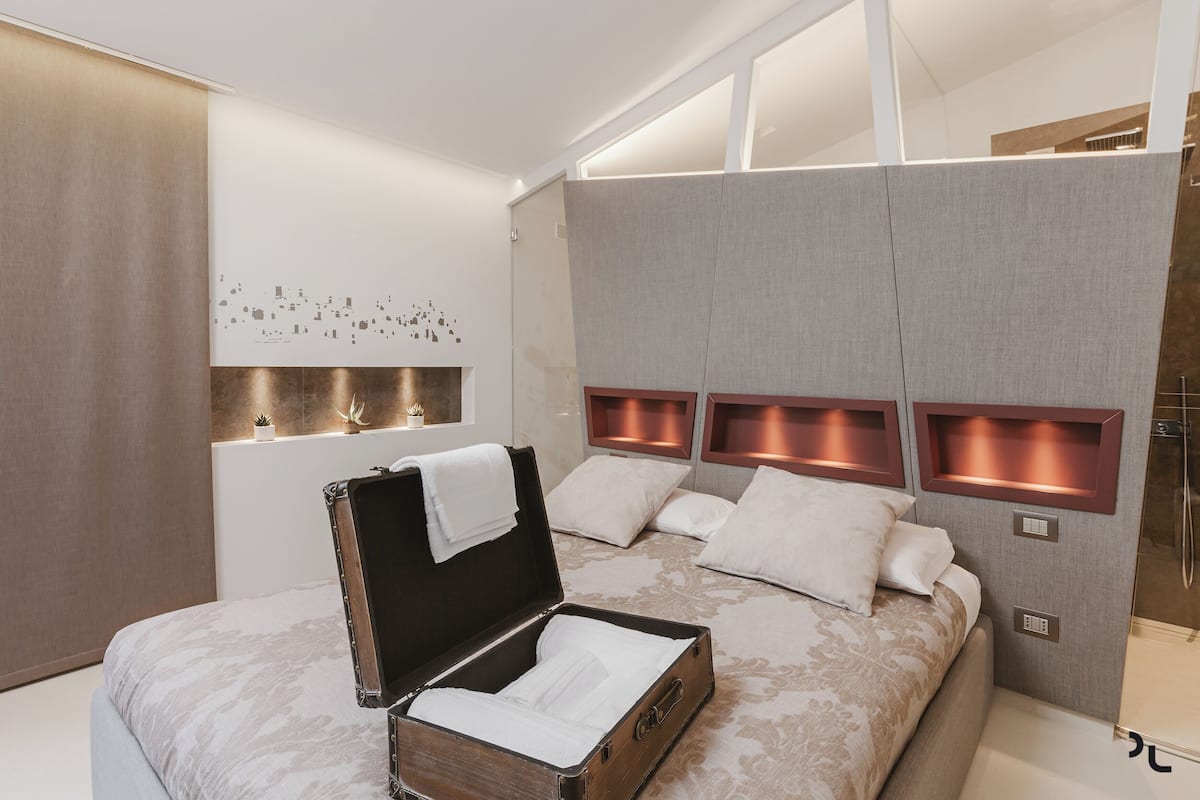 Un dormitorio moderno con una cama grande, una maleta e iluminación integrada.