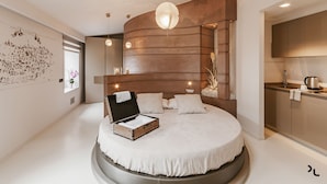 A modern bedroom with a circular bed, a wooden headboard, and a built-in kitchen area. - Residenza del Monaco Bianco (Matera)