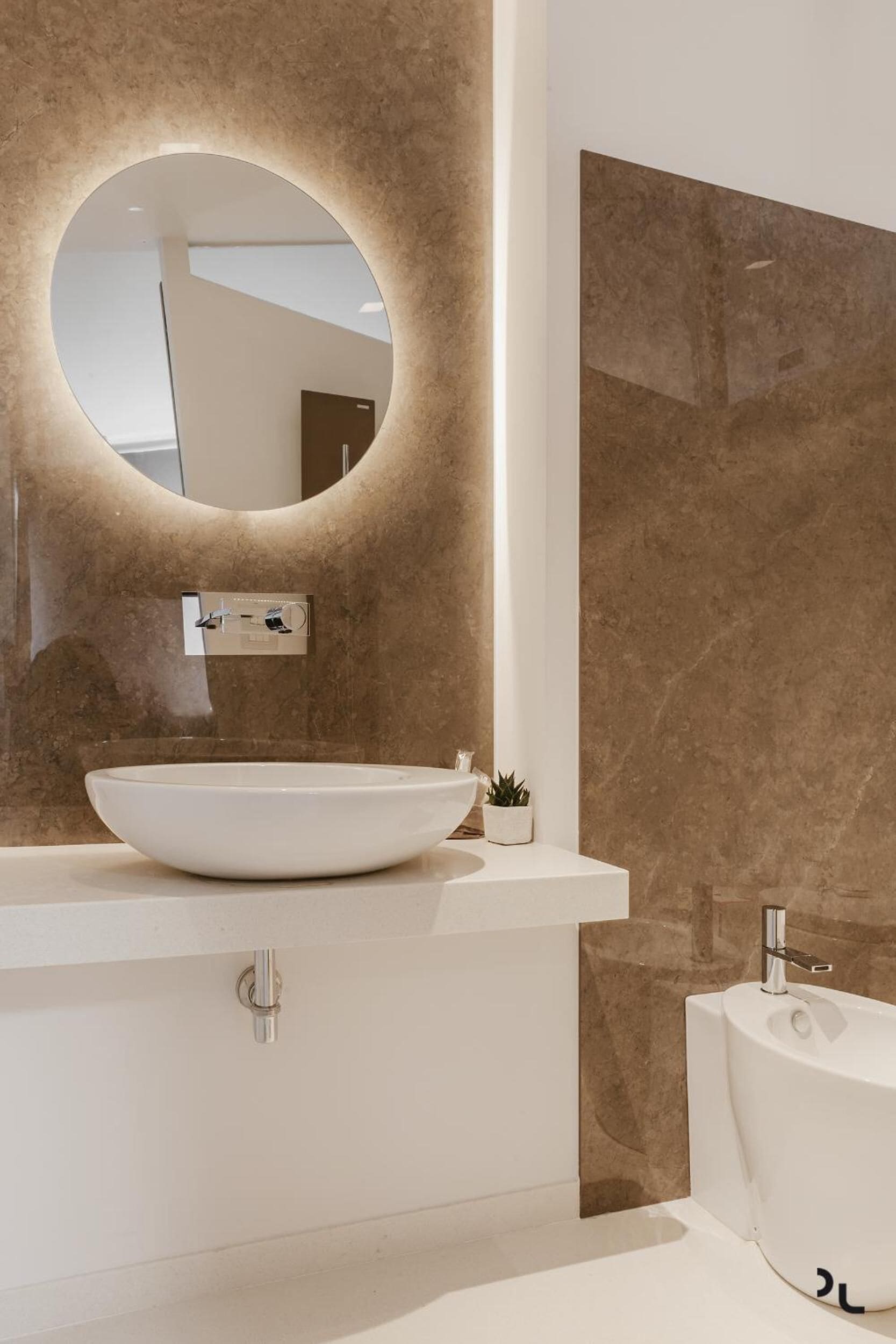 Une salle de bain moderne avec un miroir rond, un lavabo blanc et une baignoire.
