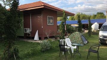 Et lille træhus med et tegltag, et telt og et bord med stole i gården.