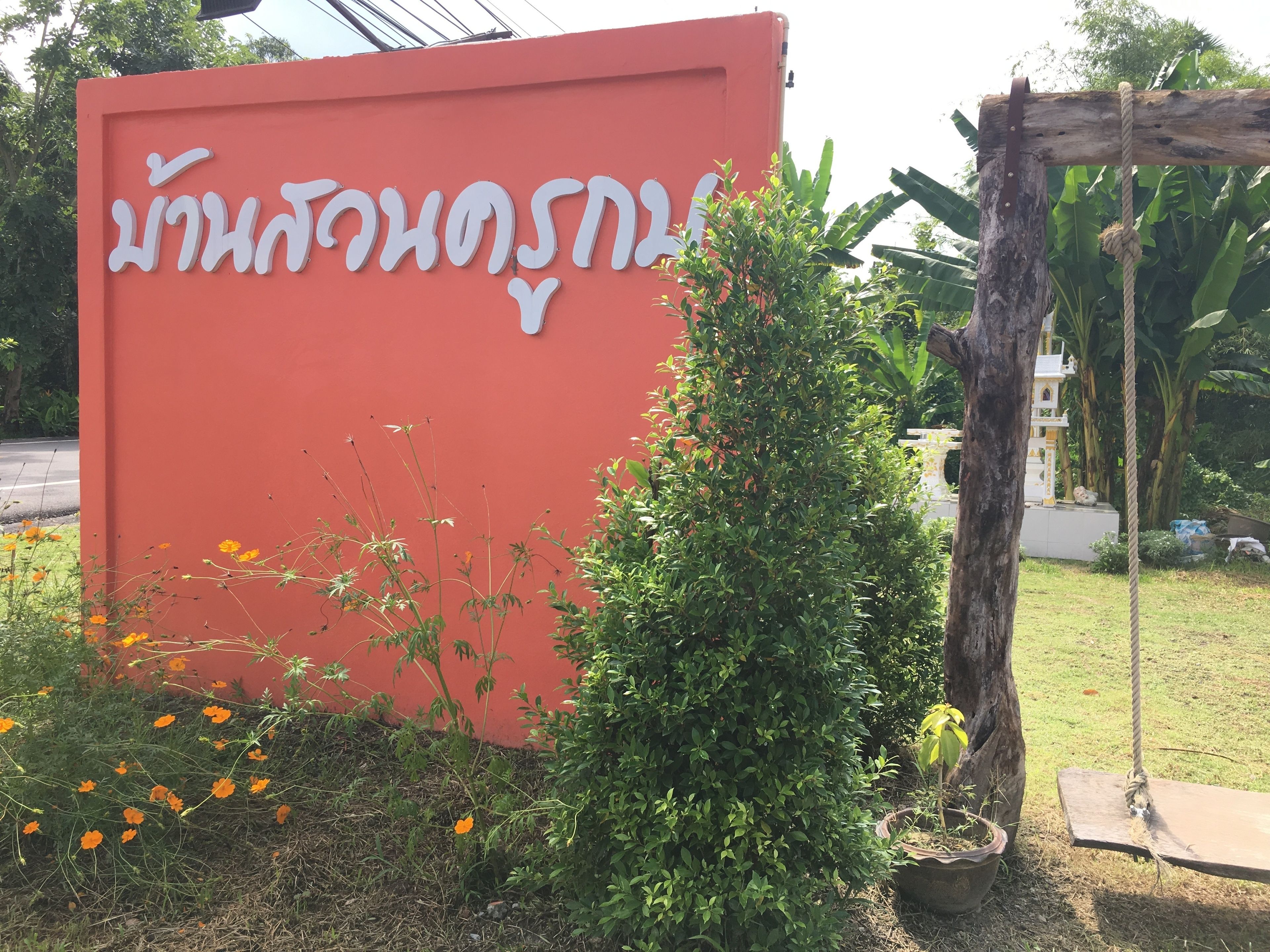A red sign with white text, surrounded by greenery and a swing set.