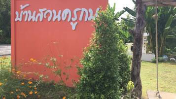 A red sign with white text, surrounded by greenery and a swing set.