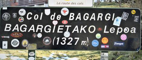 A sign with multiple stickers and text indicating 'Col de BAGARGIETAKO Lepaia' and '1327 m'.