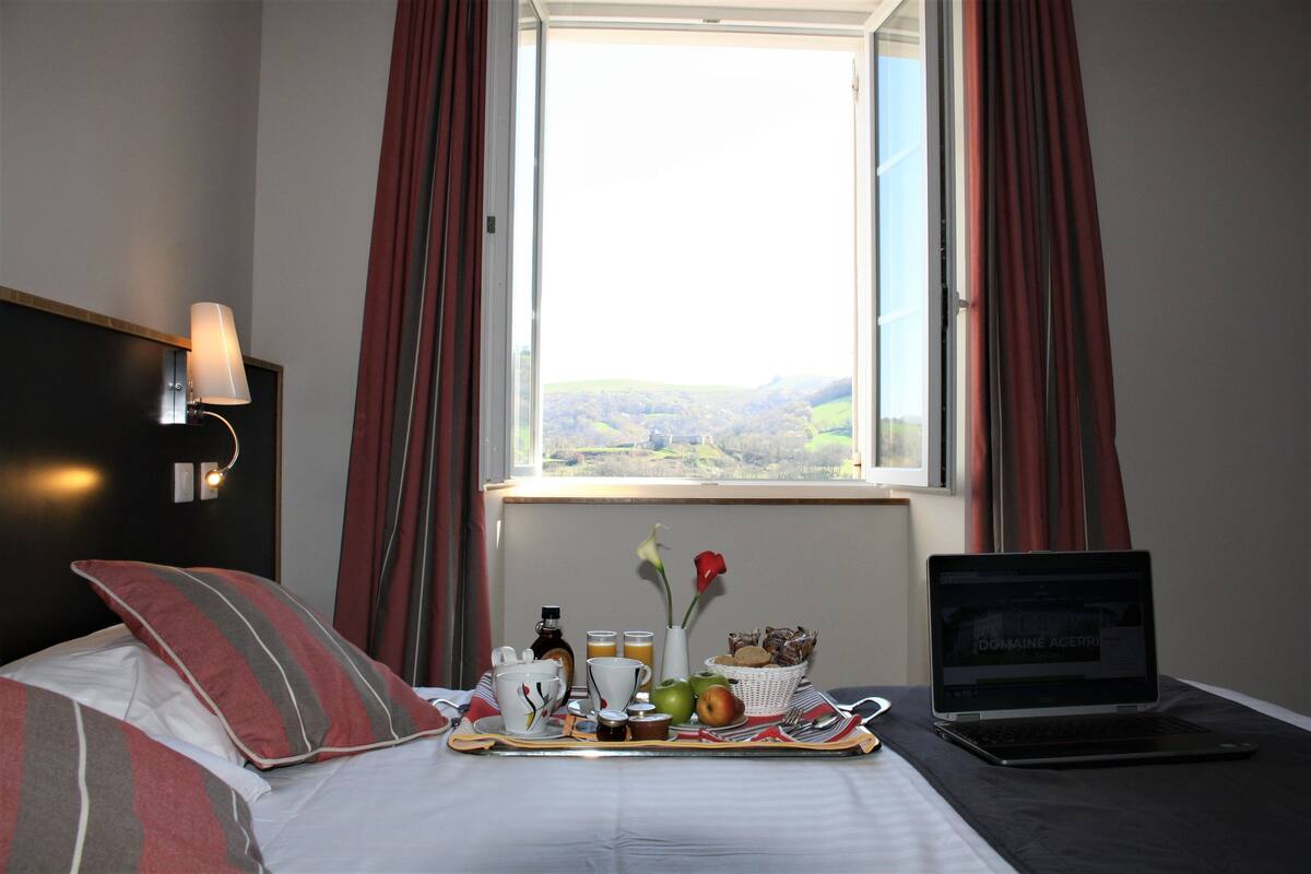 Une chambre d’hôtel avec un lit, un ordinateur portable, un plateau de petit-déjeuner et une vue sur la campagne.